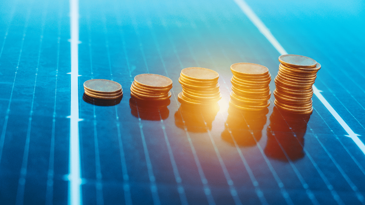 Moedas empilhadas sobre um painel solar, simbolizando o investimento e a economia na compra de energia
